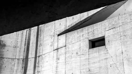 High contrast white concrete wall with dark window. Angular triangular hard shadows.