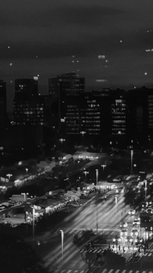 A busy city at night with lit buildings, traffic, and streetlights, in black and white.